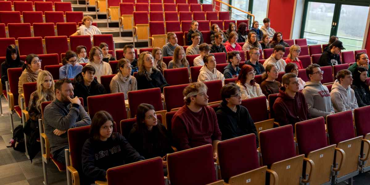 Grupa studentów siedzi w auli. Patrzą w kierunku sceny