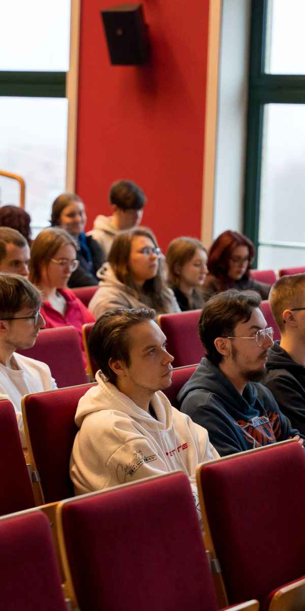 Grupa studentów siedzi w auli. Patrzą w kierunku sceny