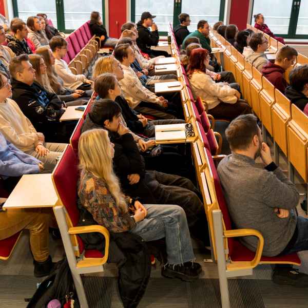 Grupa studentów siedzi w auli. Patrzą w kierunku sceny