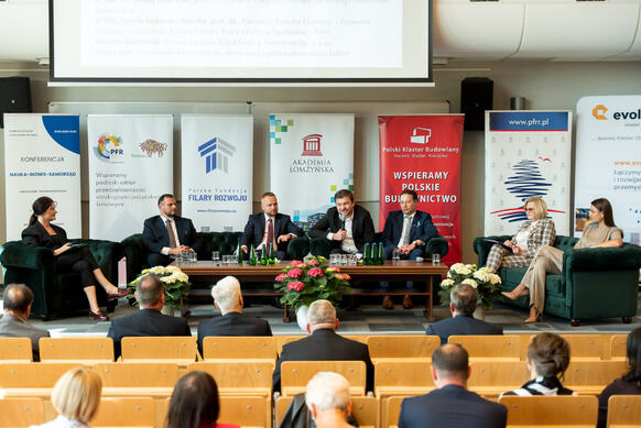Panel dyskusyjny podczas konferencji w sali wykładowej, z kilkoma prelegentami siedzącymi na scenie i publicznością w pierwszych rzędach.