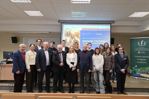 Organizatorzy i prelegenci konferencji pozują do zdjęcia grupowego. W tle baner z tytułem konferencji