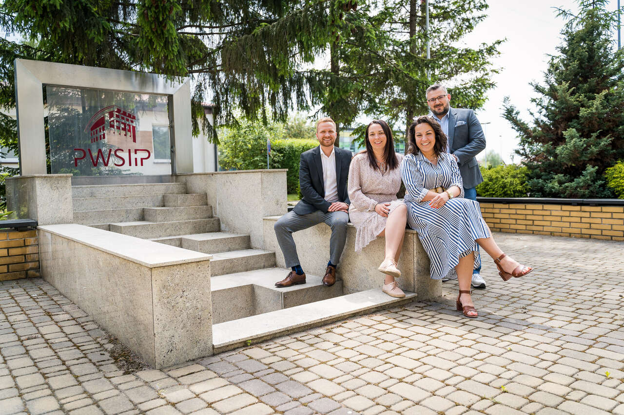 4 uśmiechniętych uczestników webinarium na tle fontanny przy ulicy Akademickiej 14 