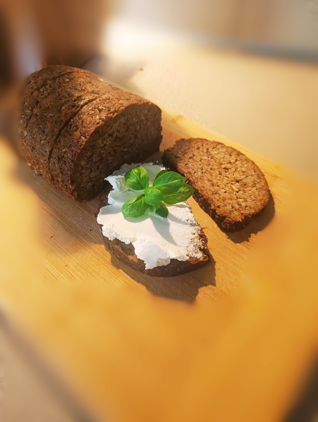 Zdjęcie przedstawia chleb na desce do krojenia i jedną kromkę chleba z twarogiem