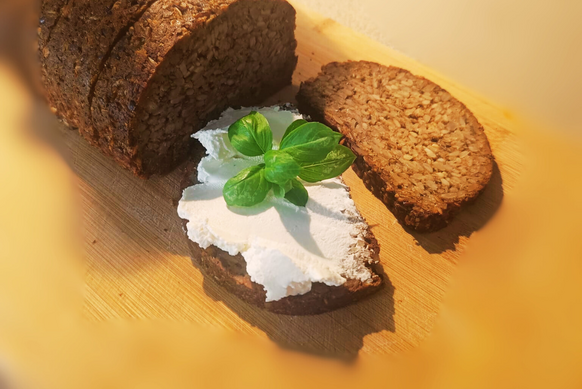 Zdjęcie przedstawia chleb na desce do krojenia i jedną kromkę chleba z twarogiem