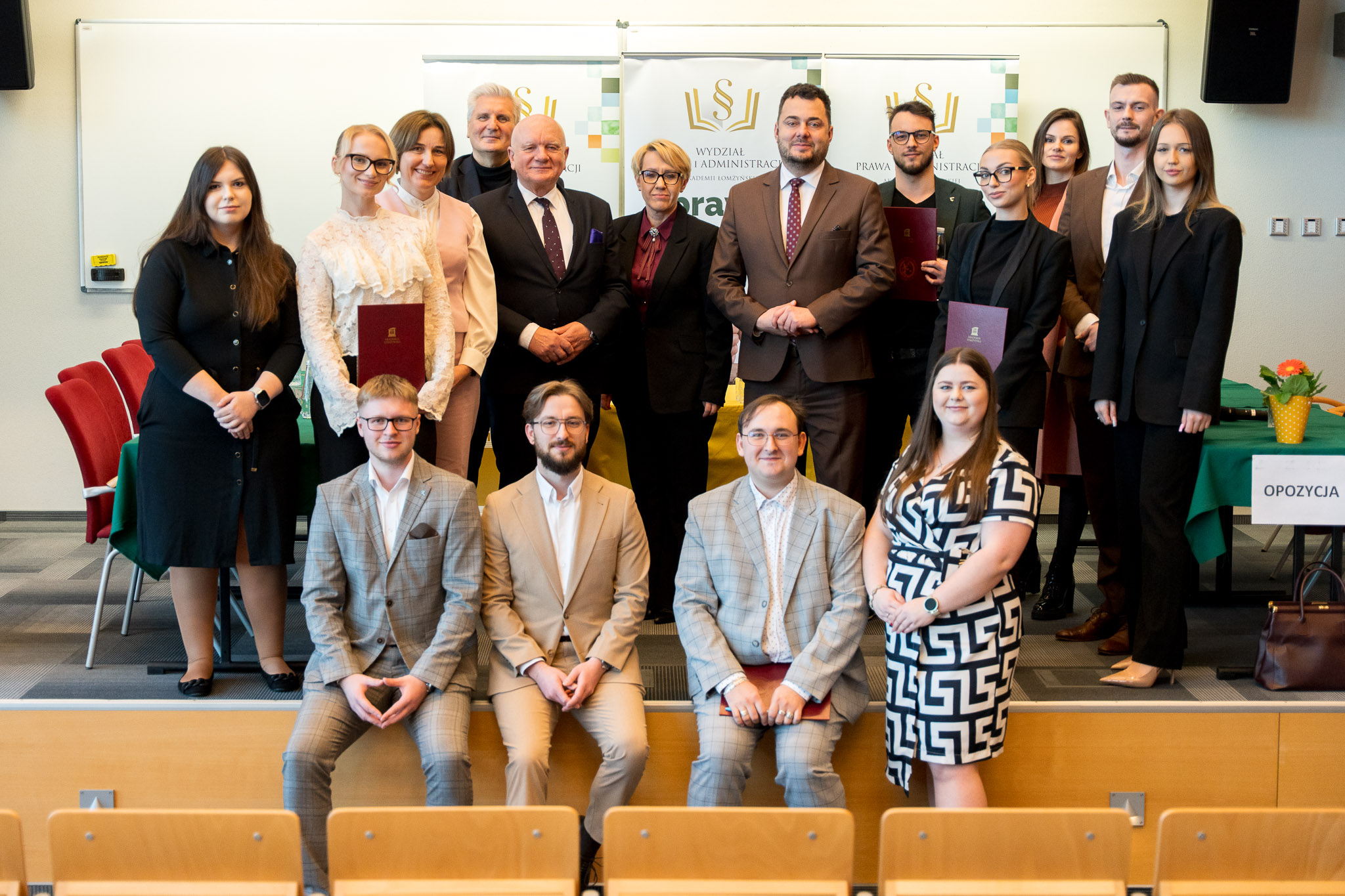Grupa ludzi pozuje do zdjęcia na podeście auli wykładowej.