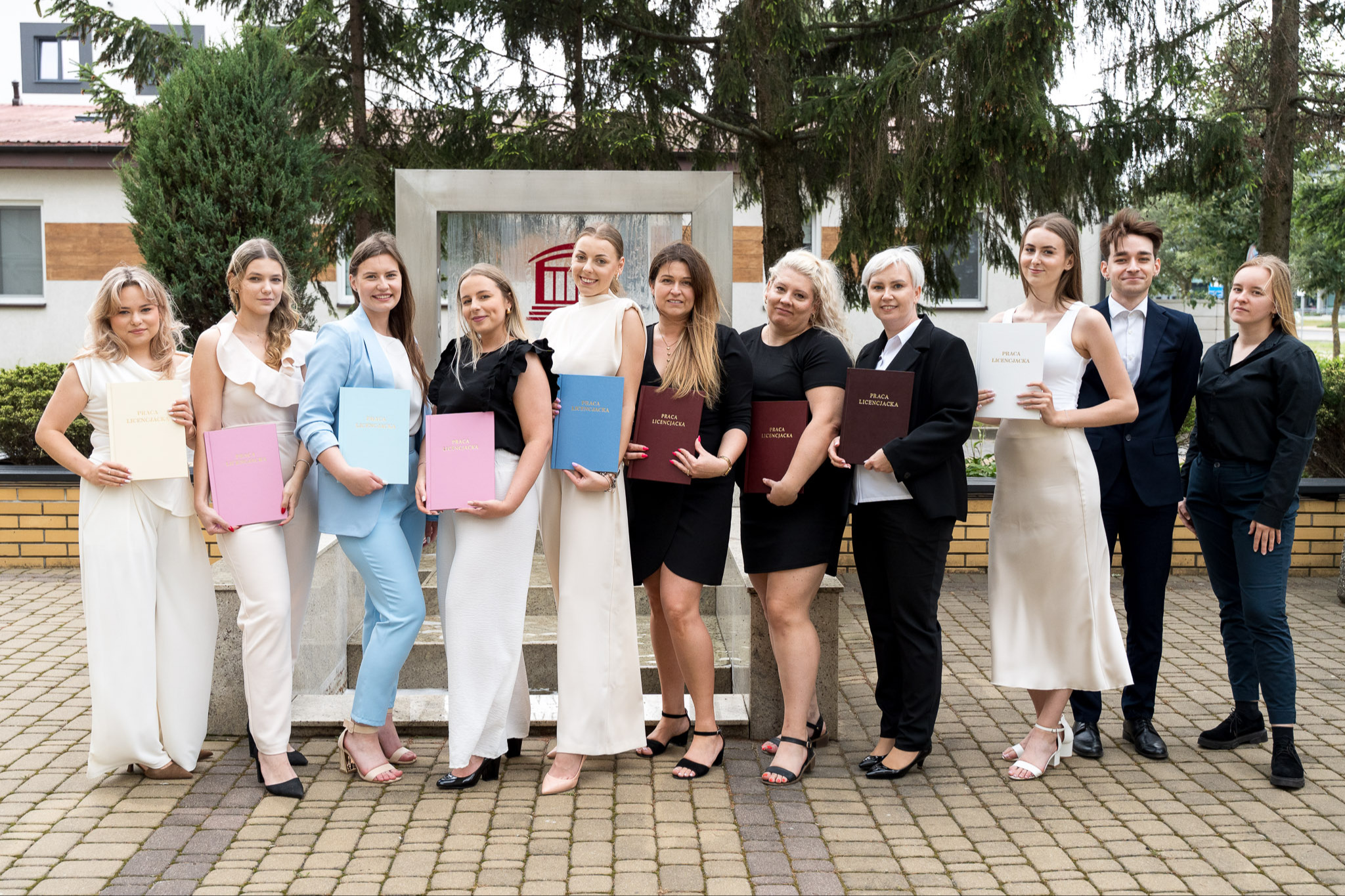 Na tle fotofontanny przy budynku Akademii Łomżyńskiej, komisja dyplomowania wraz ze studentami po obronie prac dyplomowych