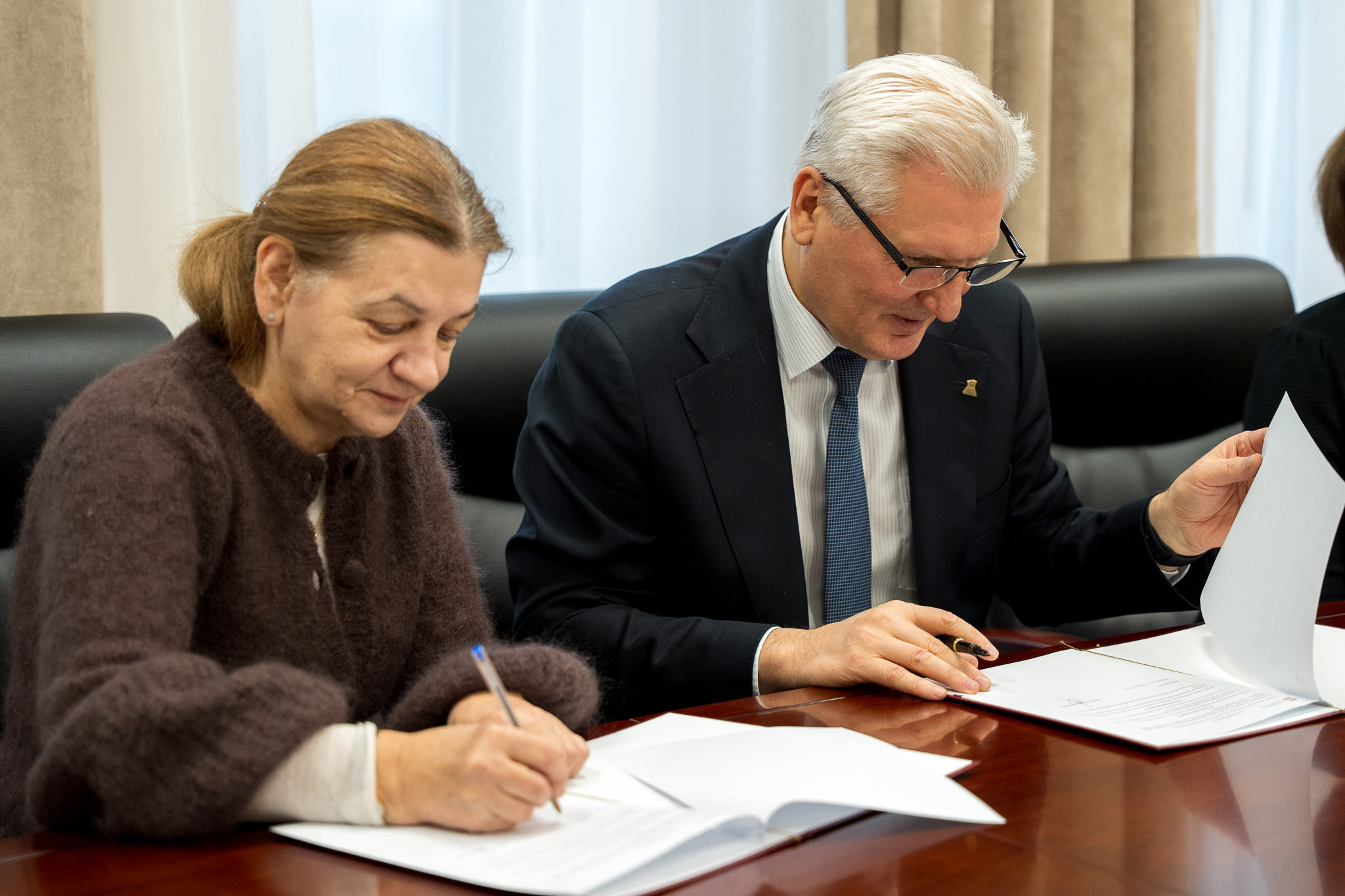 Mężczyzna i kobieta siedzą przy drewnianym stole przeglądając i podpisując dokumenty.