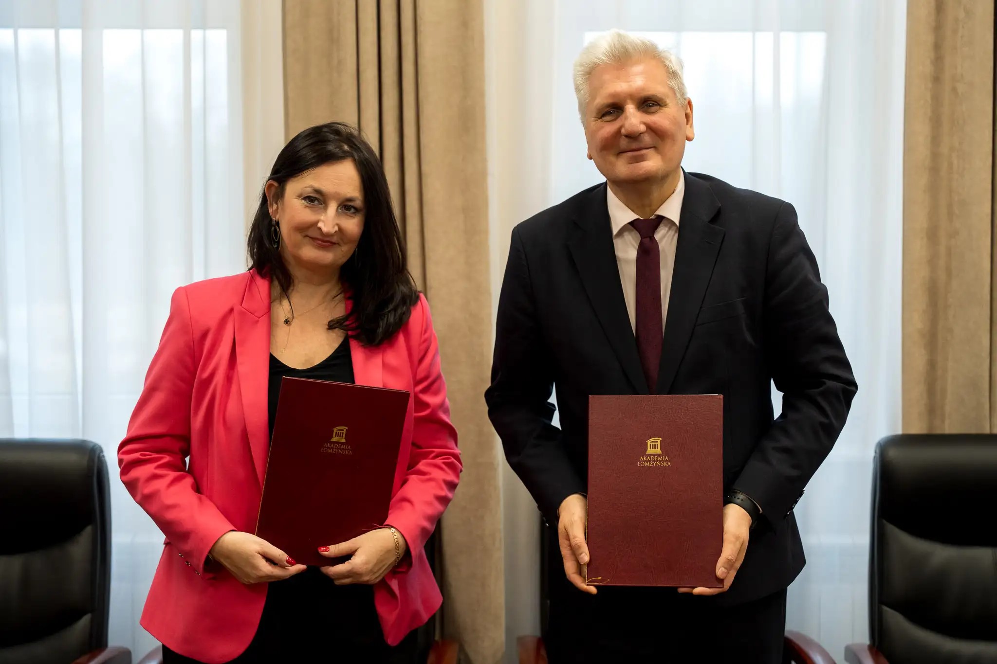 Kobieta i mężczyzna stoją za stołem konferencyjnym i trzymają w dłoniach teczki z dokumentami.