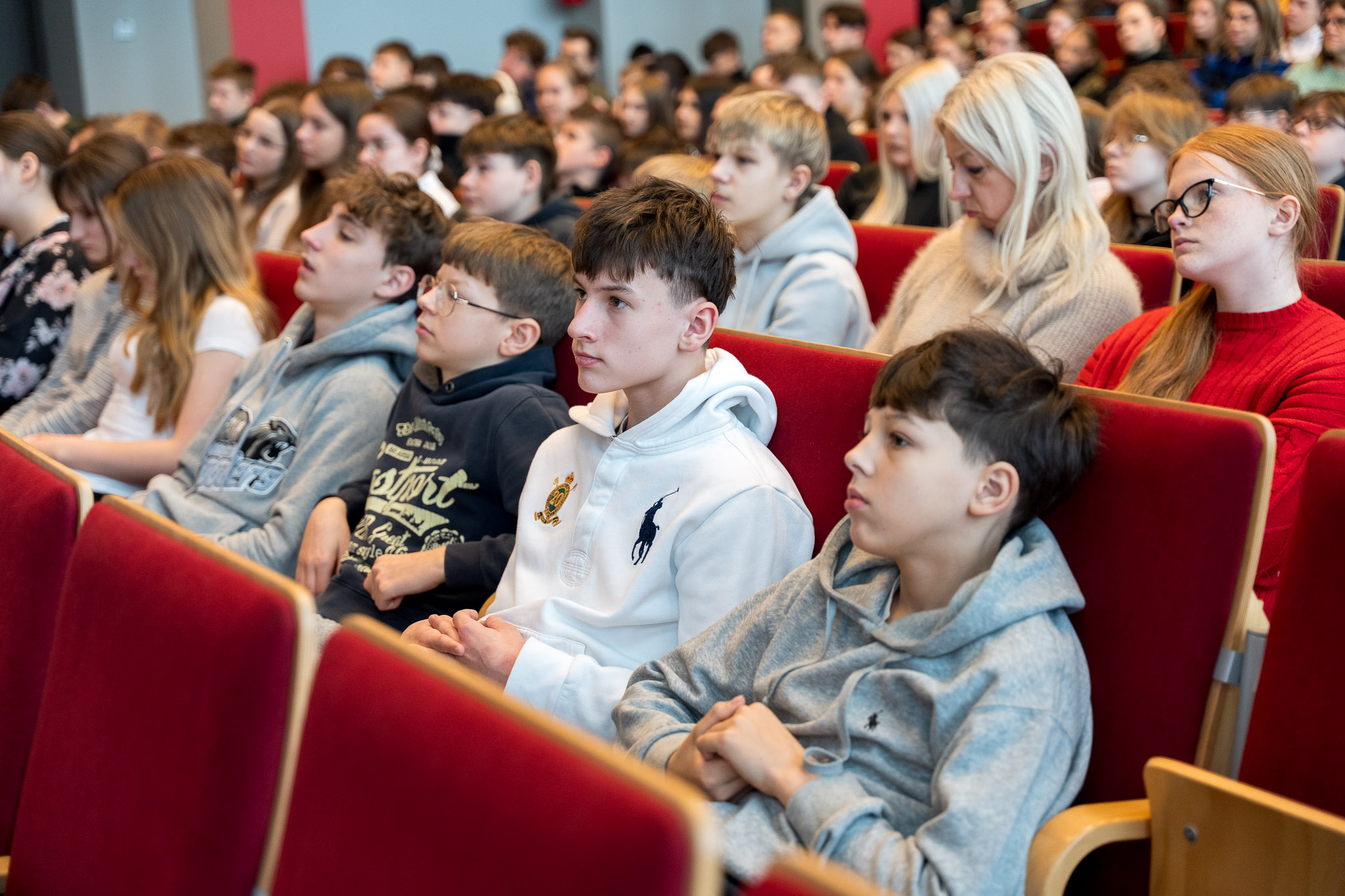 Grupa osób słucha uważnie siedząc na krzesłach w auli wykładowej.