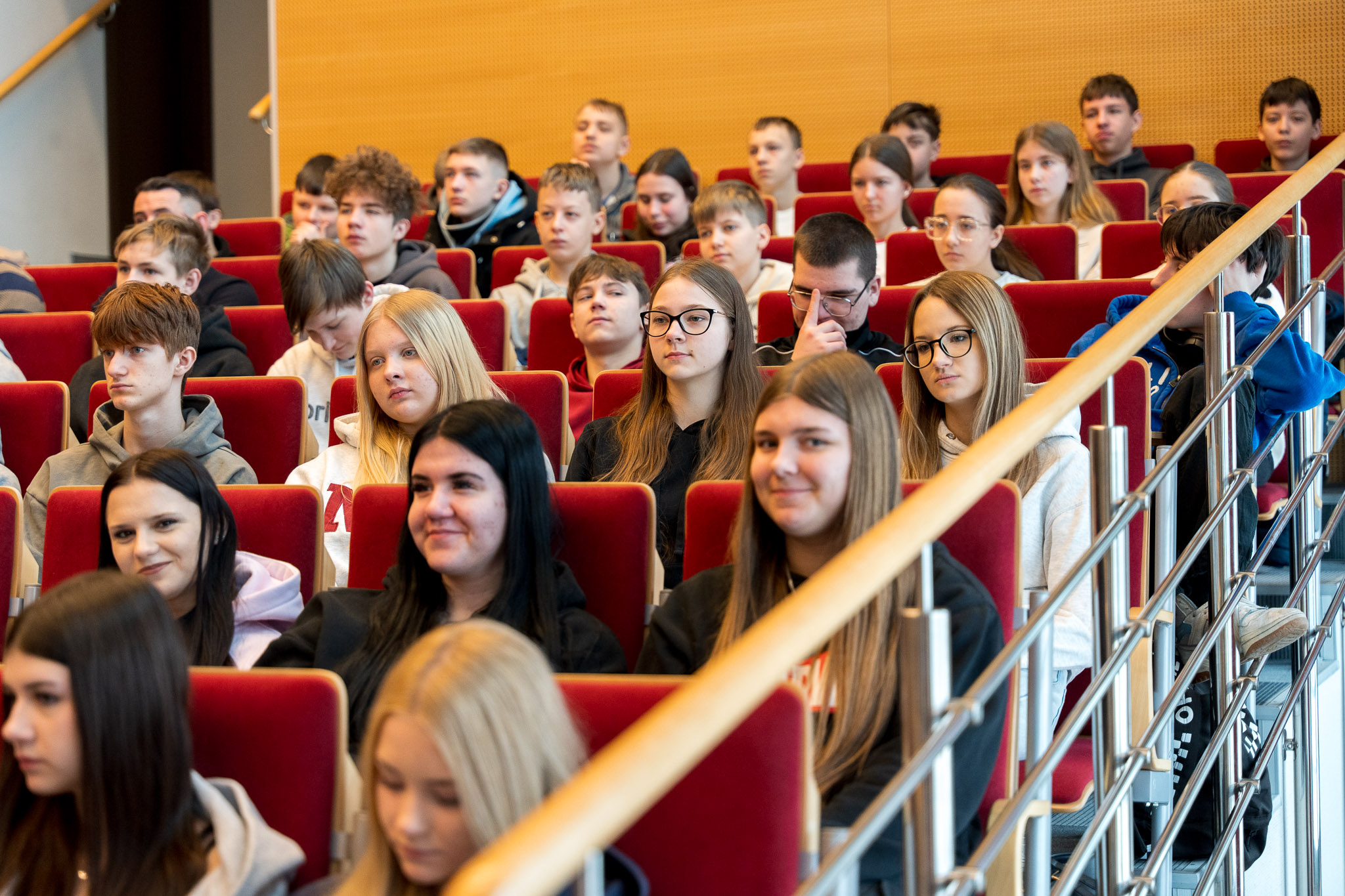 Grupa osób słucha uważnie siedząc na krzesłach w auli wykładowej.