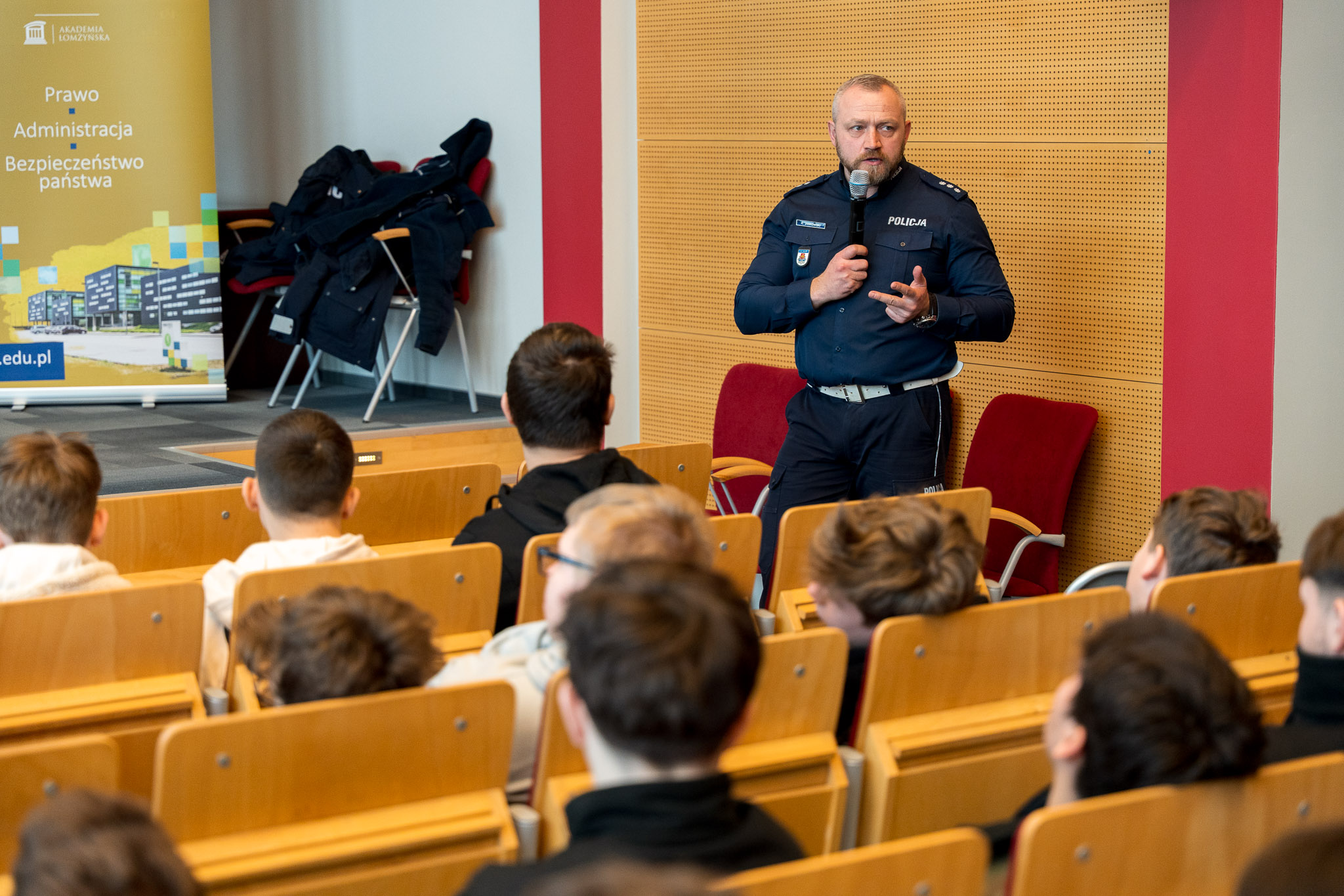 Mężczyzna w mundurze policjanta przemawia do osób siedzących na krześle w auli wykładowej.