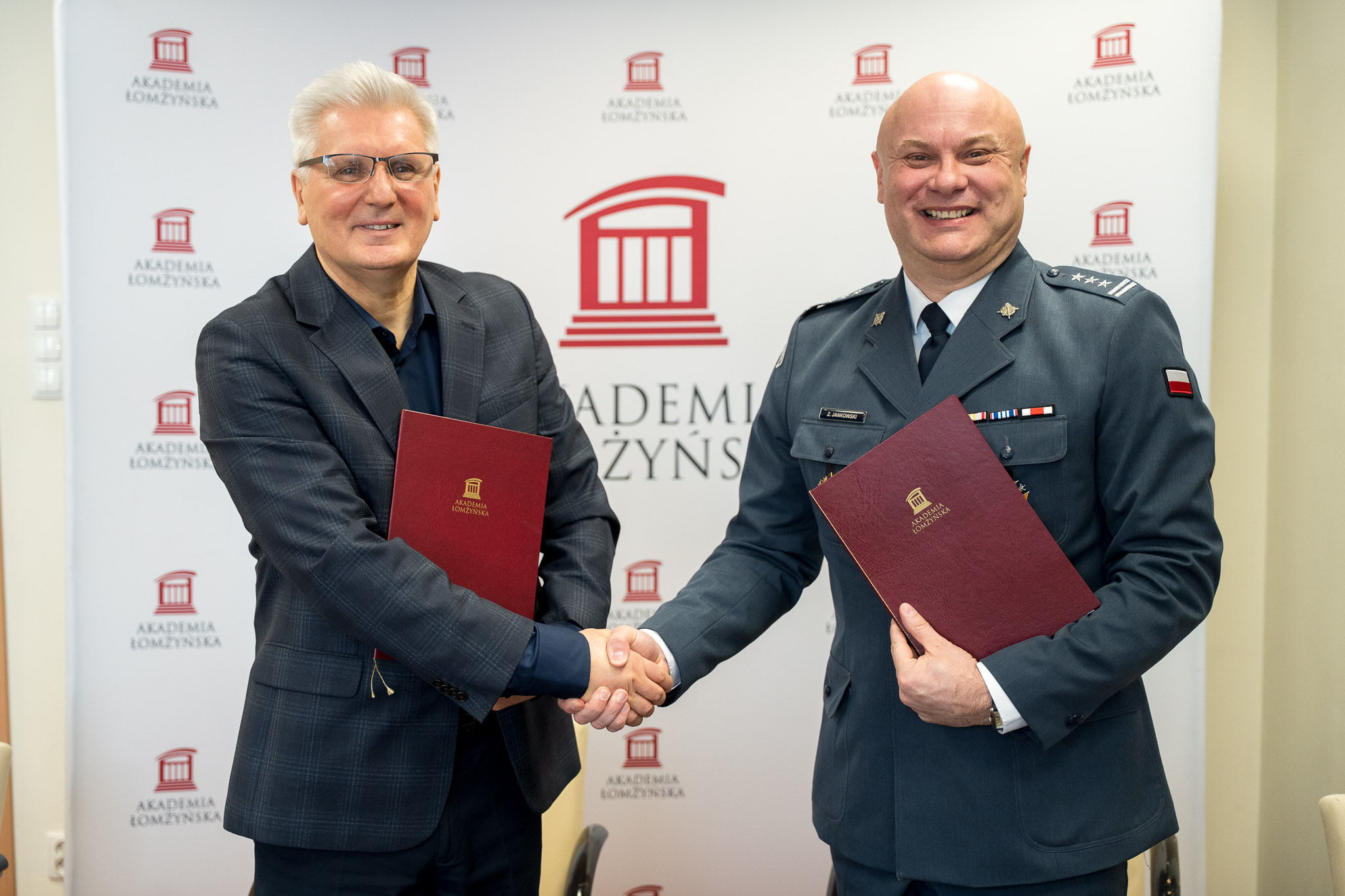 Dwóch mężczyzn stojąc podaje sobie prawe dłonie jednocześnie trzymając teczkę z dokumentami w lewej dłoni.