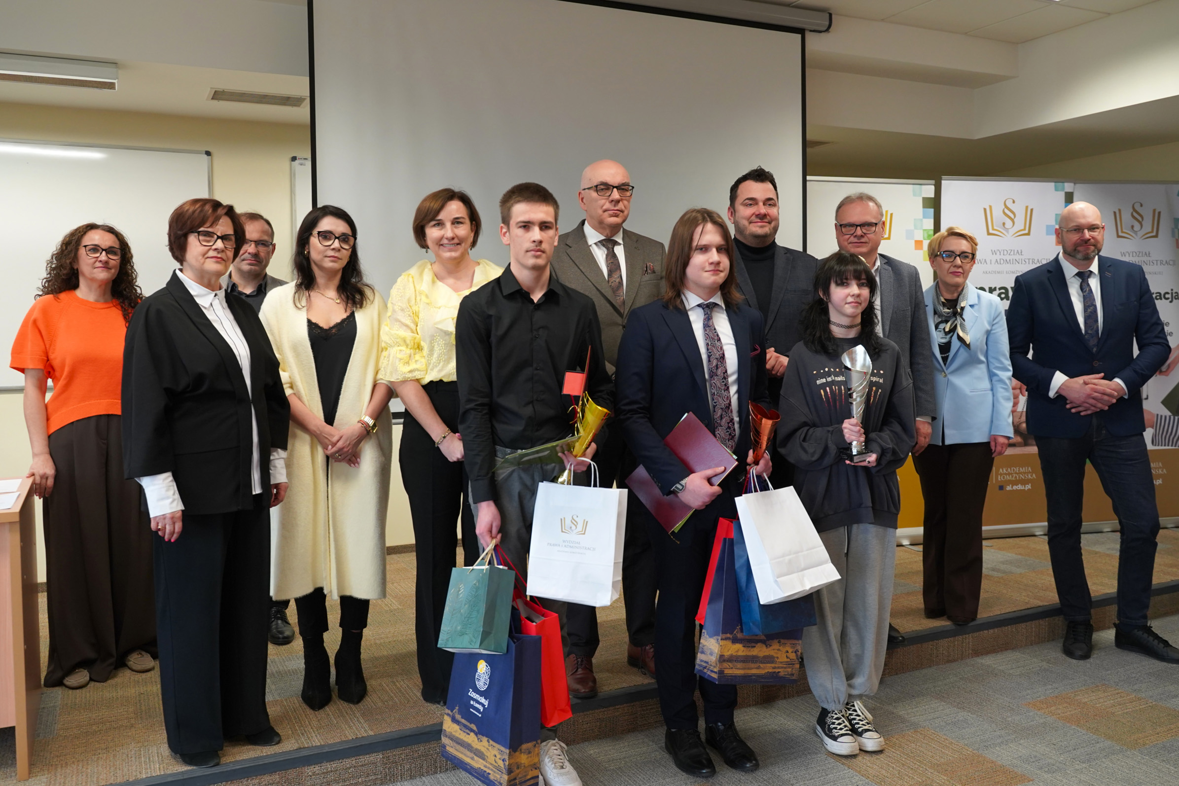 Grupa osób pozuje do zdjęcia, z przodu stoją trzy osoby z pucharami i nagrodami.