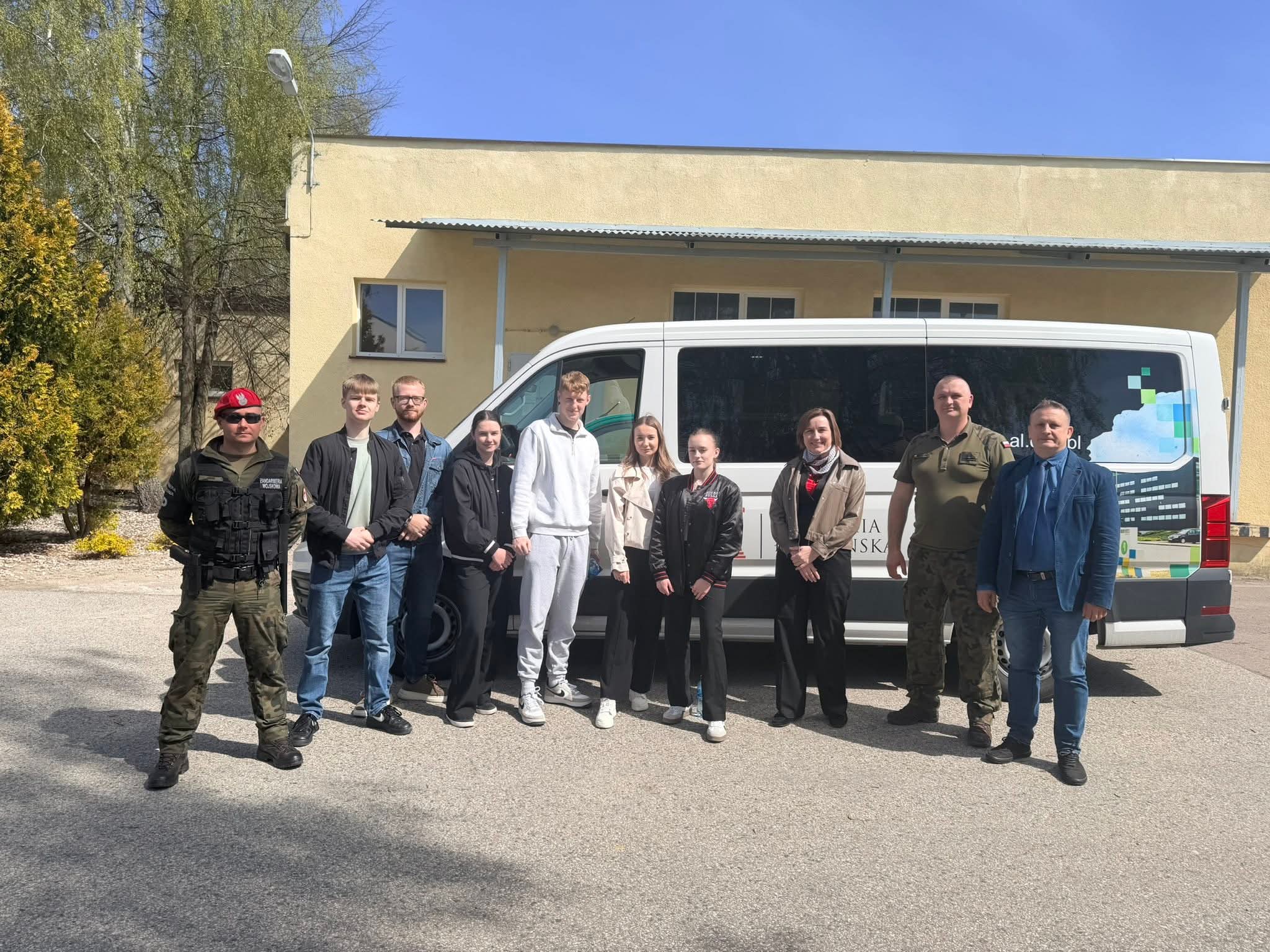 Grupa osób pozuje do zdjęcia na tle samochodu.