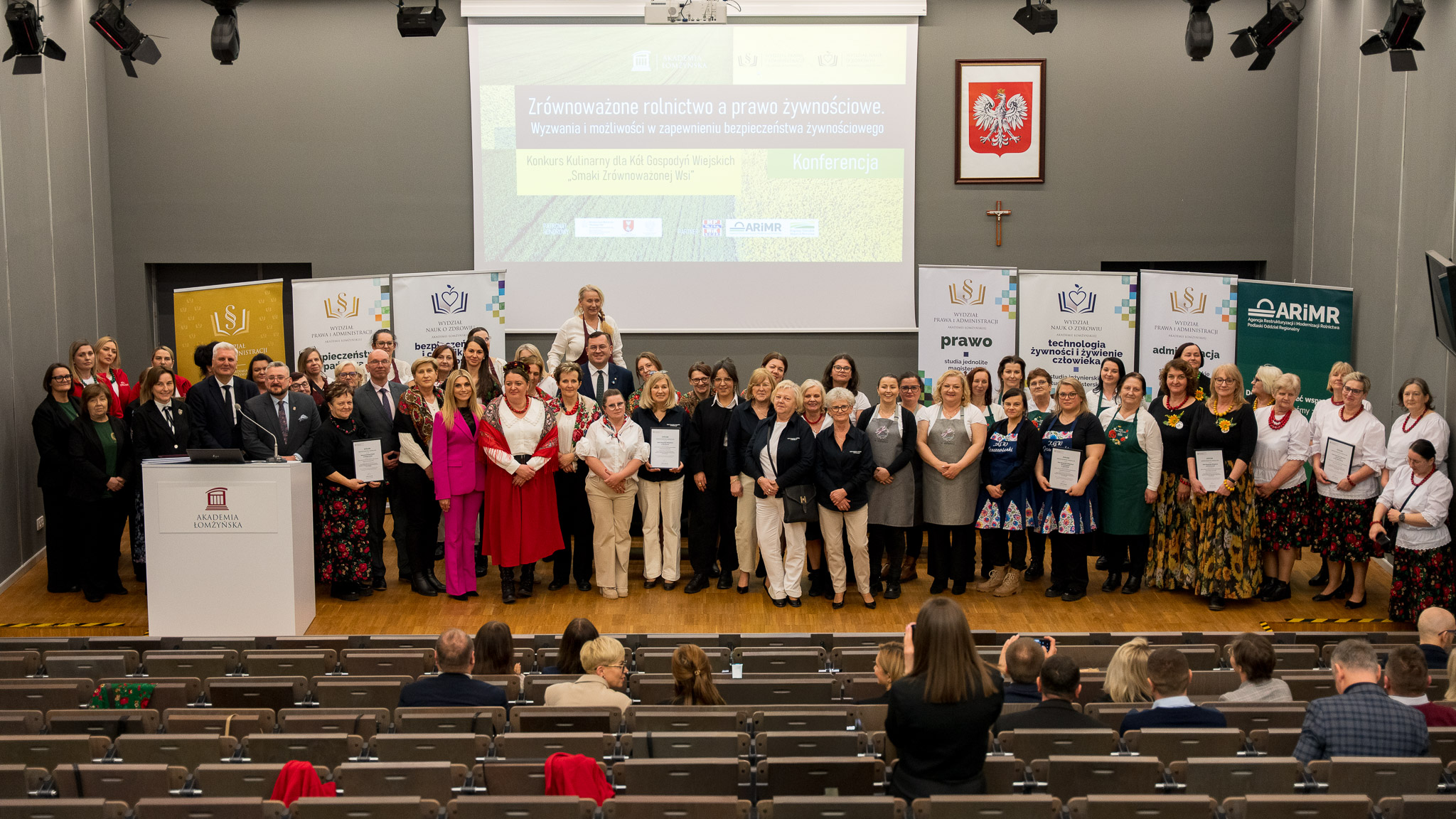 Liczna grupa osób pozuje na podium auli wykładowej.