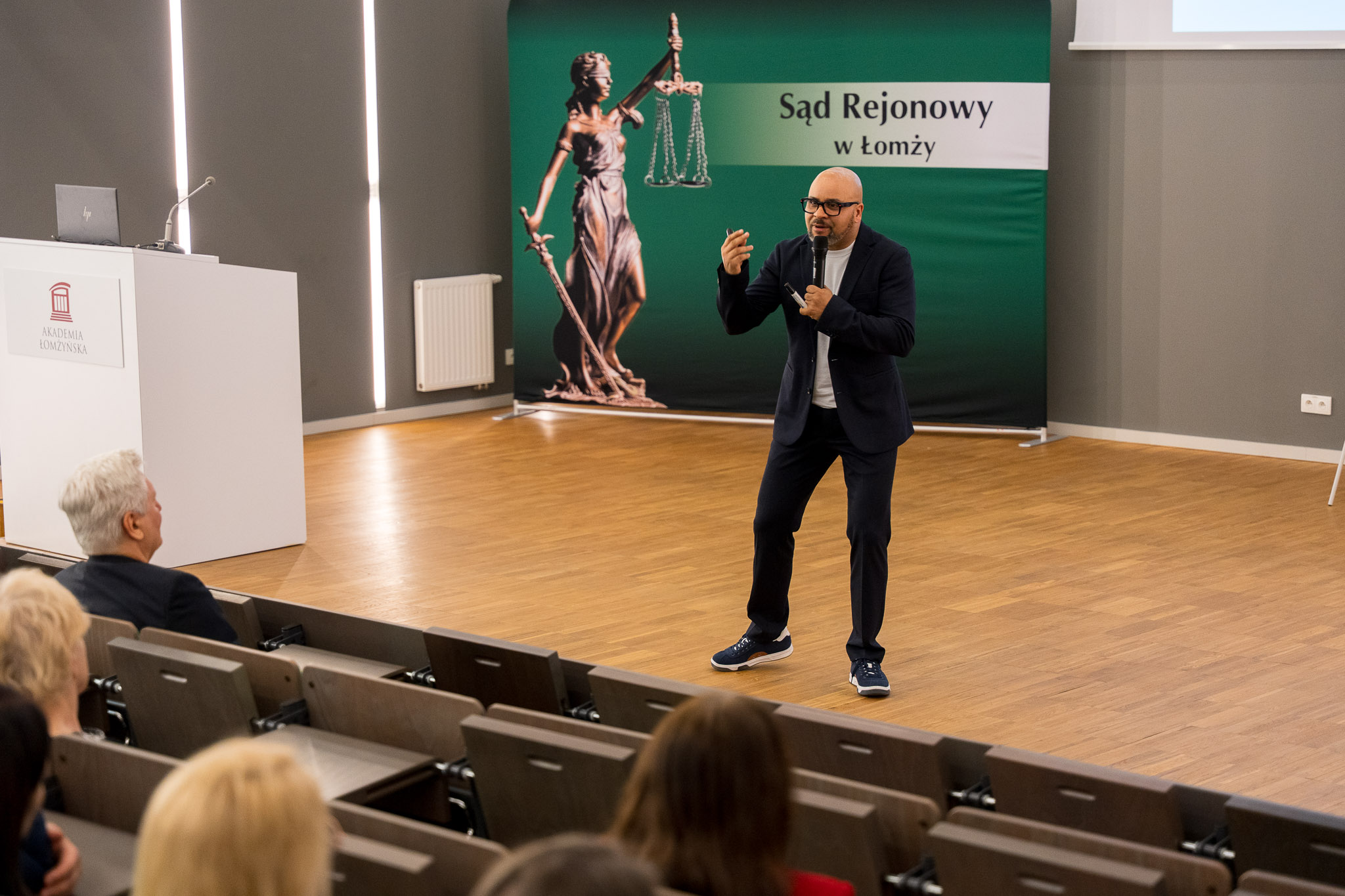 Mężczyzna wygłasza wykład z podium auli wykładowej.