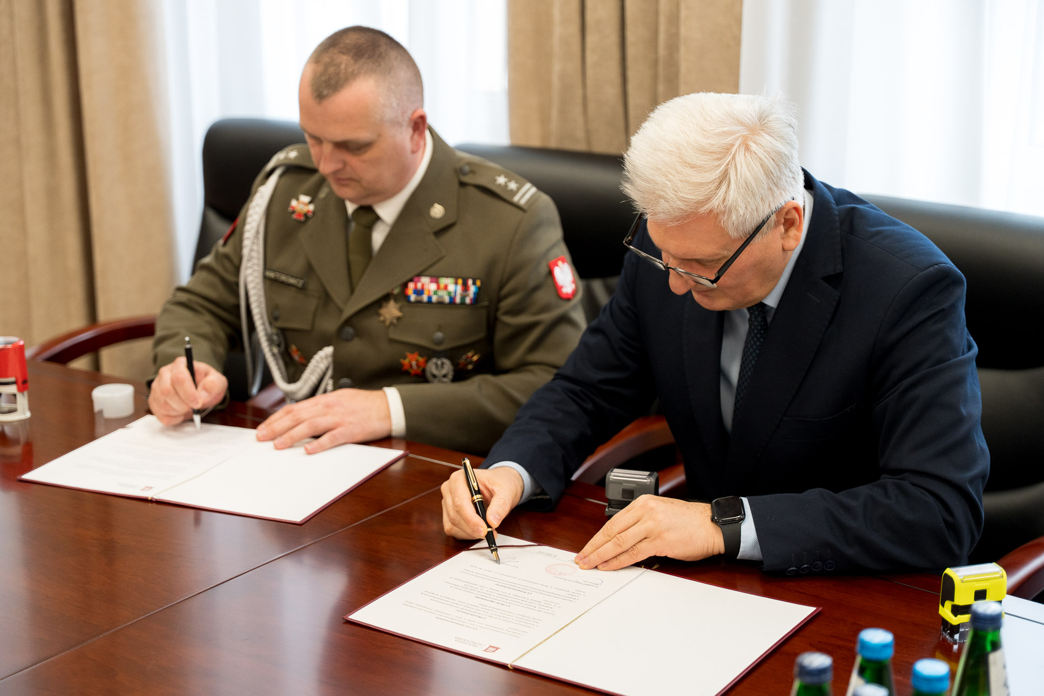 Dwóch mężczyzn podpisuje dokumenty siedząc za stołem.