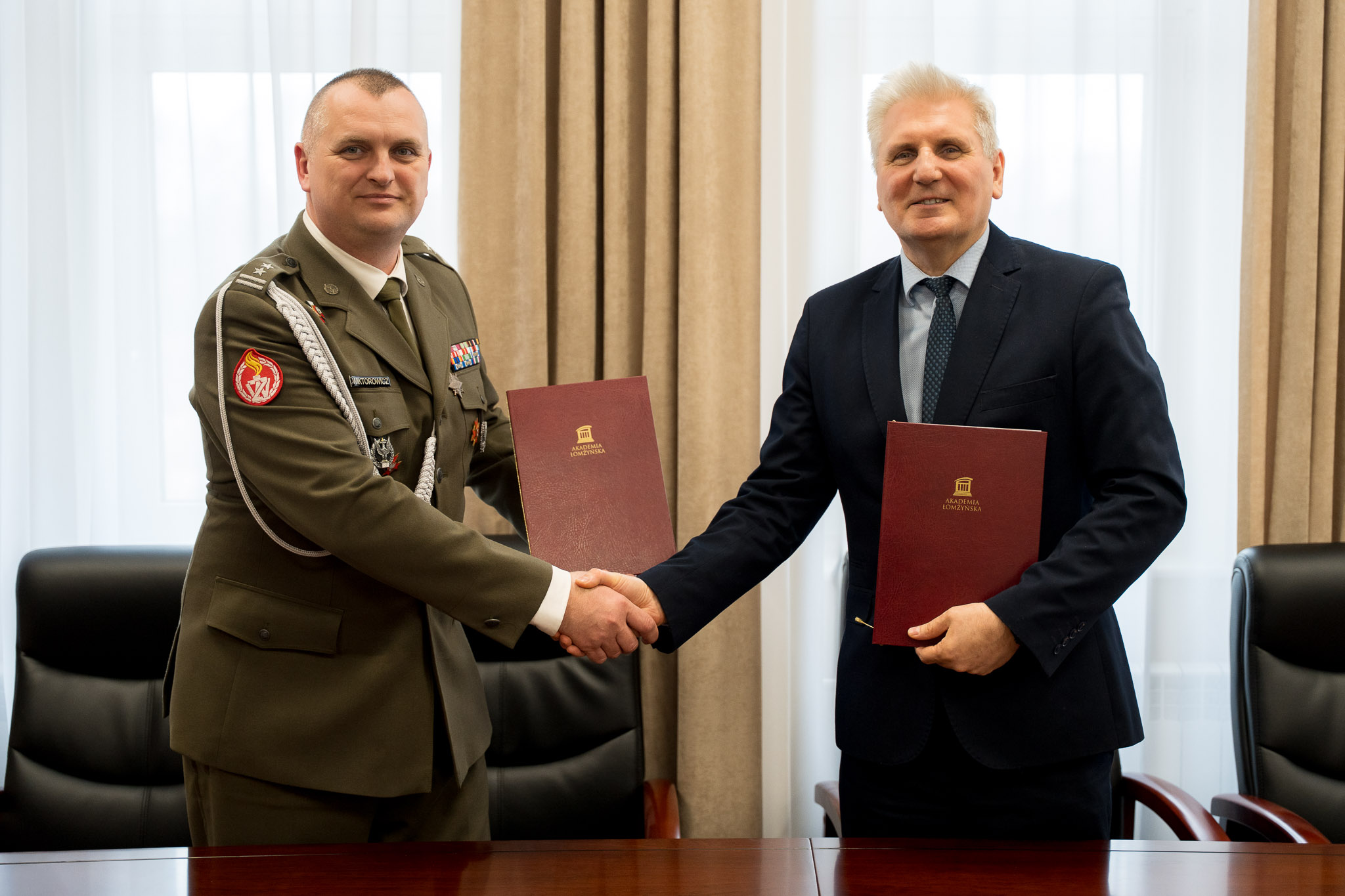 Dwóch mężczyzn uściskuje sobie dłonie trzymając w ręku teczki z dokumentami.