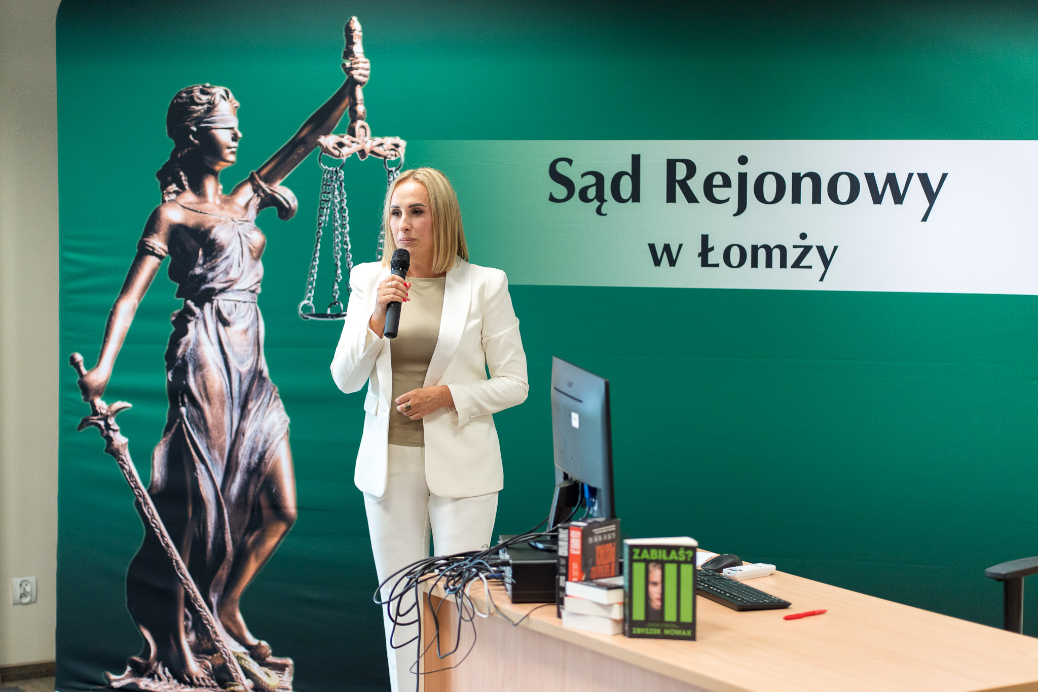 Kobieta przemawia przez mikrofon na tle logo Sądu Rejonowego.