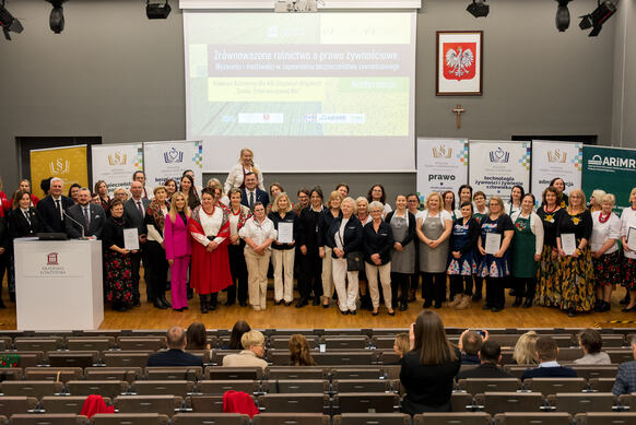 Liczna grupa osób pozuje na podium auli wykładowej.