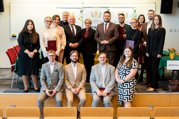 Grupa ludzi pozuje do zdjęcia na podeście auli wykładowej.