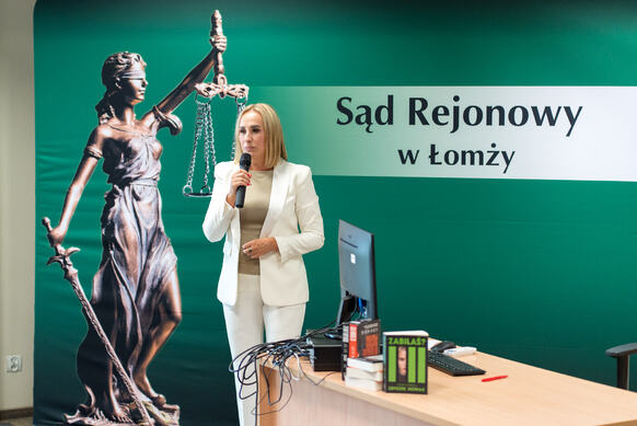 Kobieta przemawia przez mikrofon na tle logo Sądu Rejonowego.