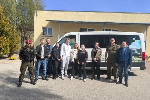 Grupa osób pozuje do zdjęcia na tle samochodu.