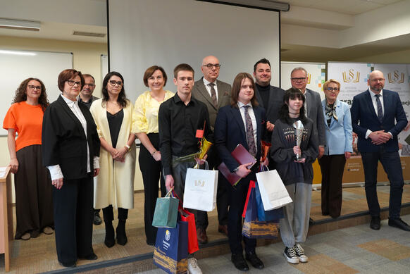 Grupa osób pozuje do zdjęcia, z przodu stoją trzy osoby z pucharami i nagrodami.