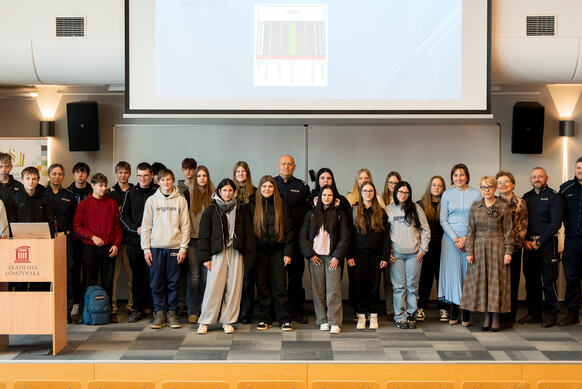 Grupa osób pozuje do zdjęcia na podeście auli wykładownej, w tle ekran projekcyjny.