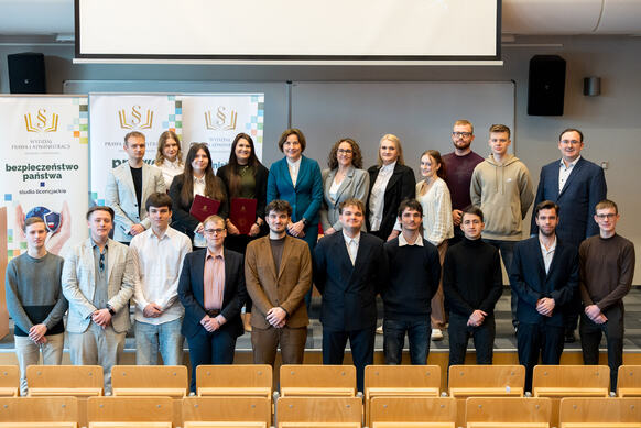 Grupa osób pozuje do zdjęcia na podeście auli wykładowej.